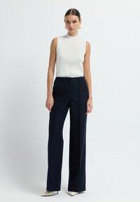 Top bianco senza maniche in maglia con texture a coste abbinato a pantaloni a vita alta a righe sottili blu navy, completato da décolleté crema con punta affilata.