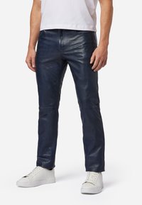 Marineblauwe leren broek met een slim fit, voorzien van een gladde textuur en gedetailleerde stiksels. Gecombineerd met witte sneakers.