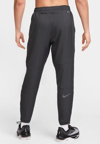 Tummanharmaat urheiluhousut, joissa vetoketjullinen takatasku, kapeutetut lahkeet ja heijastava Nike-logo. Valmistettu kevyestä, sileästä materiaalista.