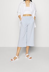 Gestreepte, lichtblauwe culottes met een brede pijp, gecombineerd met een wit cropped top en open-toe sandalen. Lichtgewicht materiaal, relaxte pasvorm.
