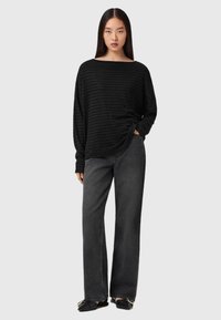 Bluză lungă cu dungi negre, cu decolteu larg, asortată cu blugi negri largi. Materialul pare moale, cu o textură subtilă.