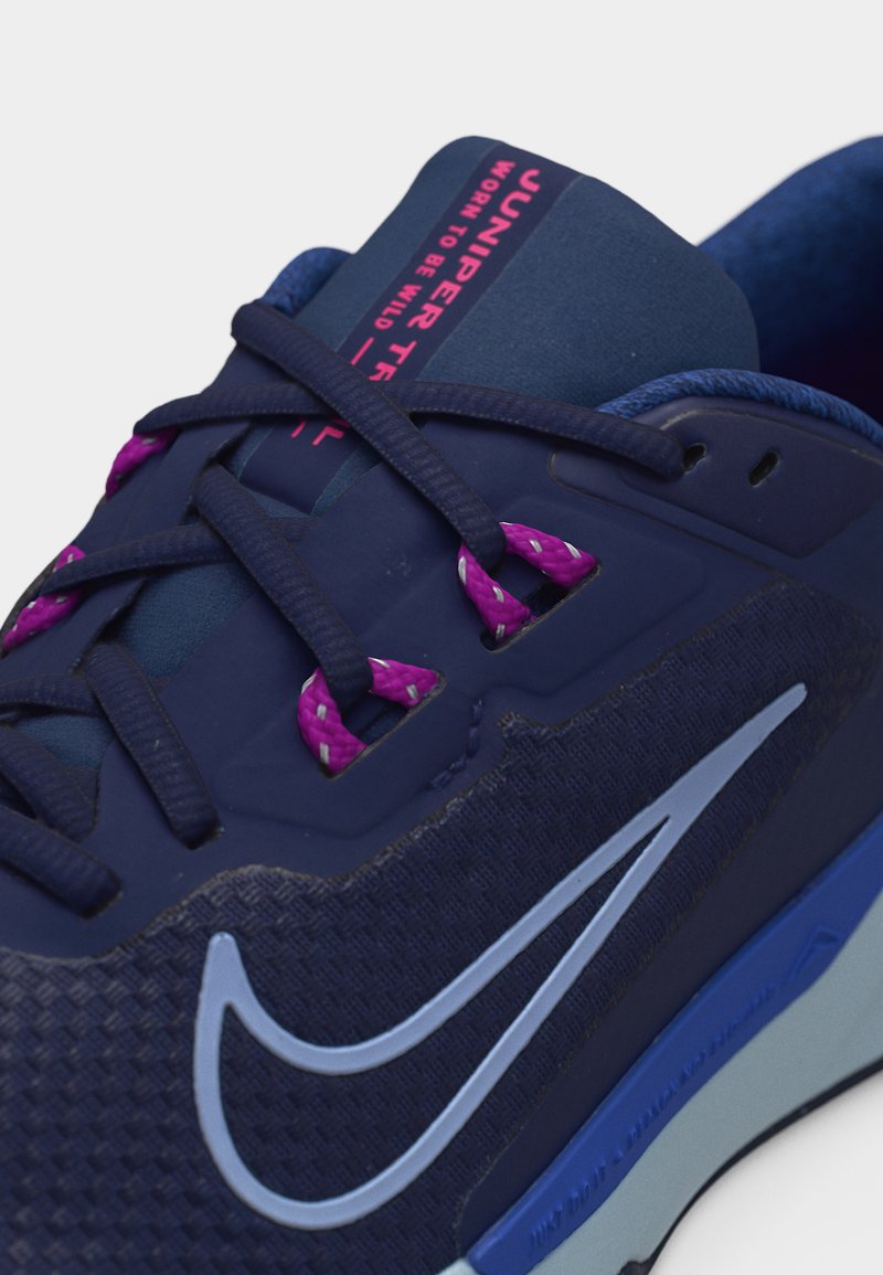 Primer plano de un zapato deportivo azul marino con cordones azul marino con acentos rosas y un logotipo de marca plateado en el lateral.