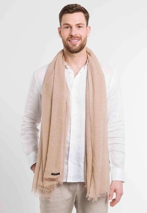 Beige textured scarf with fringed edges, worn over a white long-sleeve shirt. Notable check pattern and brand label on the side.