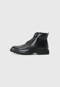Botas de cuero negro hasta el tobillo con punta redonda, cordones en la parte delantera, lados texturizados y una suela resistente para un mejor agarre. Cuenta con una pestaña trasera para ayudar a ponérselas.