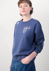 Sweatshirt bleu marine clair en coton, ornée de textes et de cœurs aux couleurs pastel, avec un col rond et des poignets côtelés.