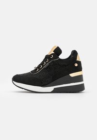 Black suede sneaker with metallic gold accents, textured mesh sides, lace-up design, and a thick white rubber sole. Features a wedge heel.