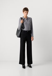 Polo gris de manga larga con rayas y botones, combinado con unos pantalones vaqueros negros de pierna ancha y alta cintura, y botas negras de tacón. Bolsa de mano negra.