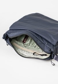 Marineblaue Tasche mit einer glatten, matten Oberfläche und einem Reißverschluss, der ein hellgrünes Innenleben zeigt. Sie verfügt über eine Innentasche und einen elastischen oberen Rand.