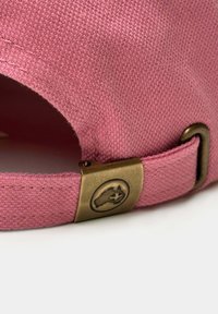 Gorra de algodón rosa con un tejido texturizado. Cuenta con un cierre de metal de latón con un logotipo en relieve y un detalle bordado en la correa.