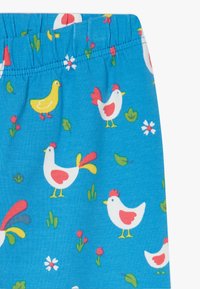 Tela azul con un estampado de gallinas y patitos amarillos, con hojas verdes y flores rojas. Cintura elástica en la parte superior.