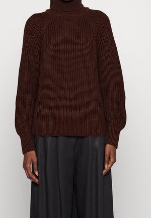 Maglione marrone lavorato a maglia con collo alto, texture a costine e maniche raglan. Abbinato a pantaloni neri ampi.