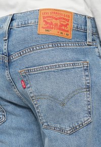 Ανοιχτό μπλε τζιν παντελόνι με δύο πίσω τσέπες και πορτοκαλί ραφή. Διαθέτει καφέ δερμάτινη πινακίδα με το λογότυπο της μάρκας και πληροφορίες για το μέγεθος.