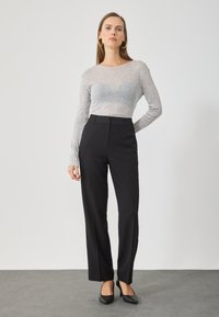 Camisola de manga longa cinza-claro com uma textura suave, combinada com calças pretas de corte elegante, com um corte reto e sem padrões visíveis. Sapatos pretos.