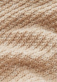 Gros plan sur un tissu tricoté beige, présentant un motif texturé avec des points en relief, créant une apparence douce et chaleureuse.