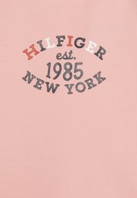 Rosa bomull t-skjorte med svart og rød tekst: "HILFIGER est. 1985 NEW YORK." Enkel design med rund hals uten ekstra mønstre.