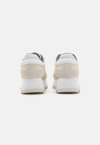 Sneaker beige realizzati in materiali scamosciati e in pelle, con una forma arrotondata, retro testurizzati e una suola piatta bianca con dettagli antiscivolo.