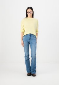 Light yellow, textured oversized sweater, paired with fitted blue denim jeans featuring slight distressing and a flared leg design. Flat, dark shoes.