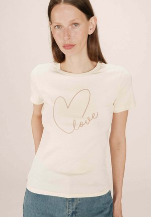 T-shirt à manches courtes de couleur crème en tissu côtelé, présentant un contour de cœur et le mot "amour" en cursif, avec un col rond.
