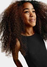 Černé šaty bez rukávů s žebrovanou texturou, které nosí osoba s objemnými, kudrnatými vlasy s hnědými melíry.