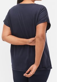 Granatowa bluzka damska z krótkim rękawem, wykonana z miękkiego materiału, o luźnym kroju i zaokrąglonym dolnym brzegu, z gładką fakturą i minimalnymi konturami.