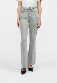 Svetlo sive razširjene kavbojke z visokim pasom, s sprednjimi žepi in subtilno teksturo. Kombinirane s črnimi čevlji z ozkim koničastim prsti.