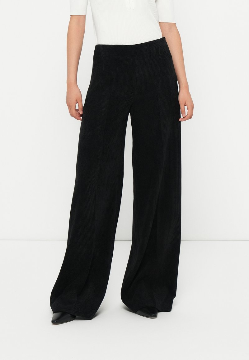 Black wide-leg corduroy pants with a textured surface and a high waistband. Pairing with pointed black shoes completes the look.
