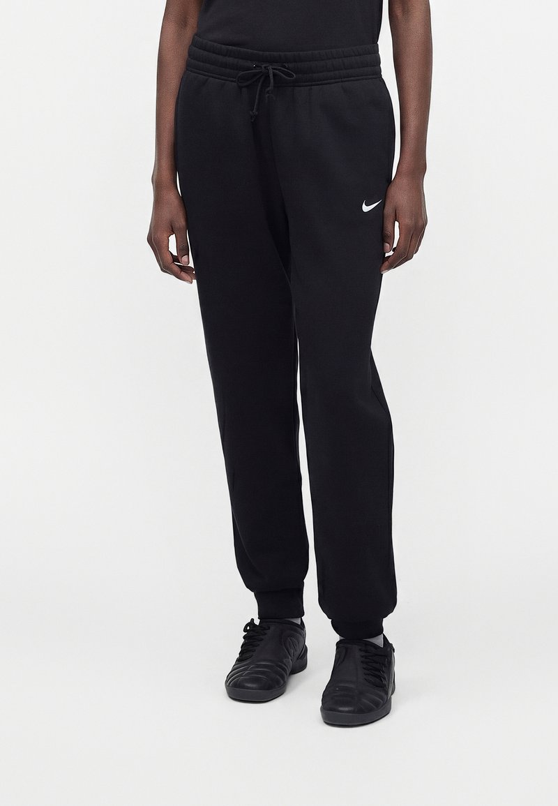 Person trägt schwarze Nike Sweatpants mit elastischem Bund und Kordelzug, kombiniert mit schwarzen Sneakern und einem schwarzen Oberteil.