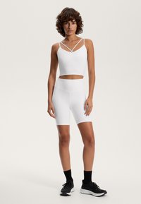 White cropped top with dual straps and matching high-waisted bike shorts. Fabric appears smooth and stretchy, paired with black athletic shoes.