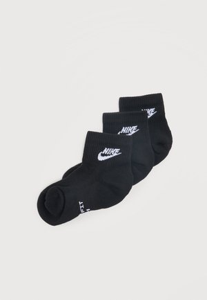 Trois paires de chaussettes courtes noires avec des logos Nike swoosh blancs empilées sur un fond gris clair.