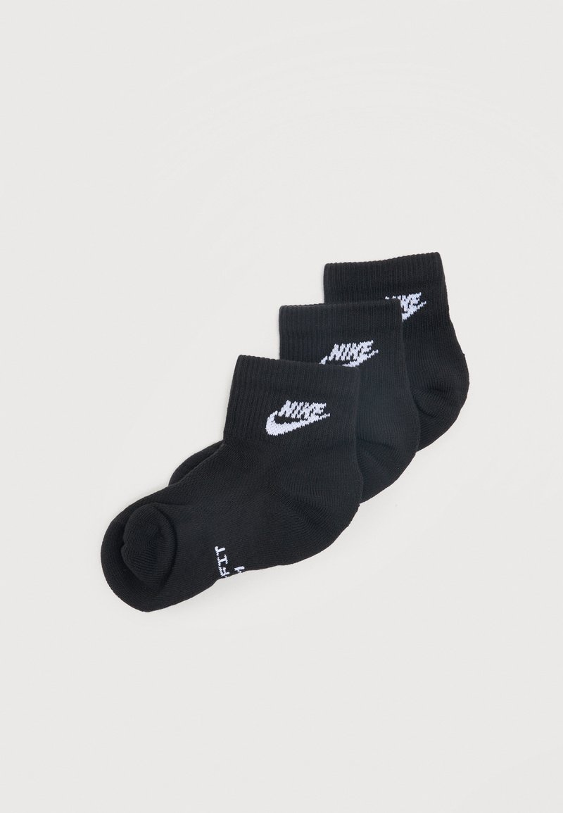 Trois paires de chaussettes courtes noires avec des logos Nike swoosh blancs empilées sur un fond gris clair.