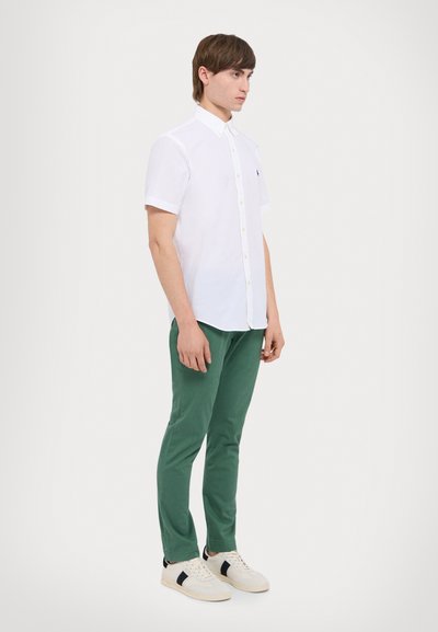 Chemise blanche à manches courtes avec patte de boutonnage, associée à un pantalon vert et des baskets blanches avec des accents noirs. Design simple et ajusté.