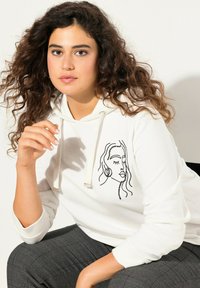 Felpa bianca con un disegno a linea nera del volto di una donna sul lato sinistro del petto. Il tessuto è liscio, dotata di cappuccio con cordino e polsini a coste.