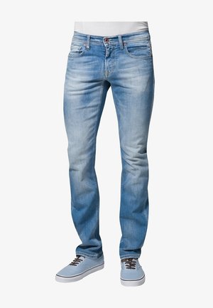 Lichtblauwe slim-fit jeans gedragen met lichtblauwe sneakers en een wit shirt, zichtbaar van taille tot voeten op een witte achtergrond.