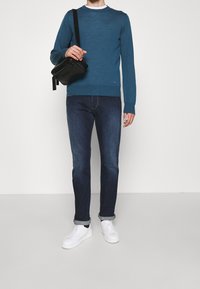 Teal crew-neck sweater, dark jeans, white sneakers, and a black crossbody bag. Sweater features texture, jeans are fitted, shoes are smooth.