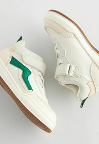 Hvide og cremefarvede høj-top sneakers med et grønt bølge-design på siden, struktureret overflade, Velcro-stropper og en brun gummisål.