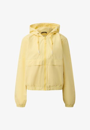 Żółta kurtka z kapturem zapinana na zamek błyskawiczny, ze sznurkami ściągającymi, elastycznymi ściągaczami na rękawach i w pasie, przedstawiona na jednolitym białym tle.