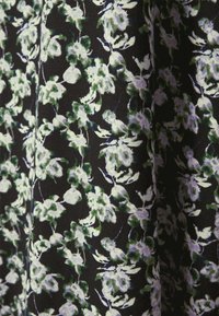 Gros plan sur un tissu avec un petit motif floral blanc et vert sur fond noir, montrant la texture et les plis.