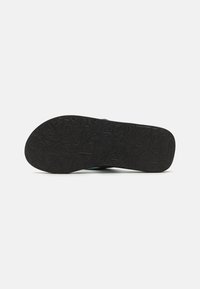 Schwarze Schuhsohle mit strukturiertem Muster und geometrischen Designs; flache Form mit glatter Oberfläche. Das Gesamtdesign ist sportlich und funktional.