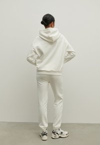 Biała bluza z kapturem i pasujące dresy. Miękka tkanina, luźny krój, ściągacze na mankietach oraz regulowany kaptur. Noszone z masywnymi sneakersami.
