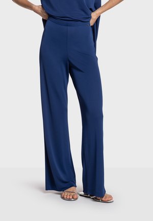 Marineblå bukser med brede ben i blødt stof med en glat tekstur. Har elastik i taljen og slidser for bevægelsesfrihed. Sølvdetalje ved taljen.