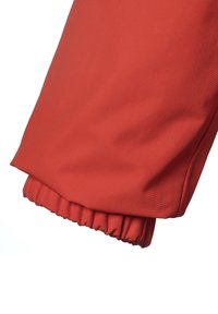 Röd, elastisk manschett på ärmen av en jacka tillverkad av texturerat syntetiskt material, med en slät yta och rynkad detalj vid handleden.