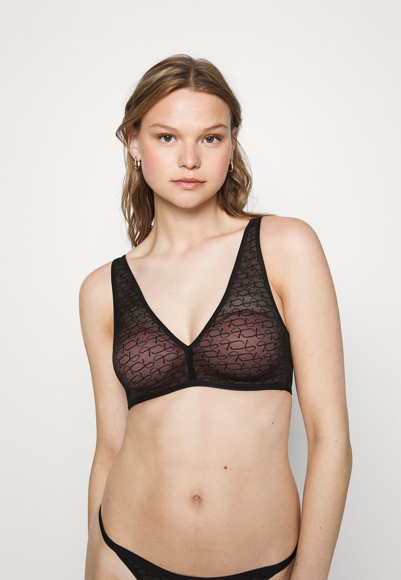 Svart bralette med et gjennomsiktig stoff som har et repetert mønster. Designet inkluderer en V-hals og brede stropper for støtte.