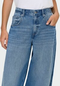 Jeans cu picioare largi de culoare albastru deschis, fabricati din denim, avand talie inalta, buzunare frontale si o textura usor decolorata.