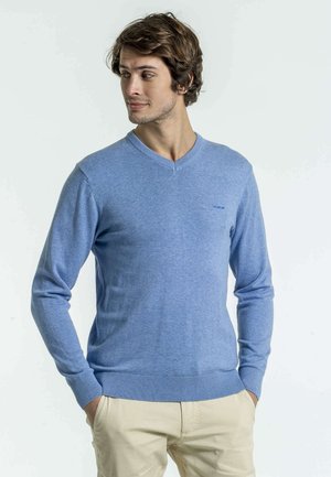 Pull en tricot bleu clair avec un col en V, des poignets et un ourlet à côtes, présentant un petit logo sur la poitrine.