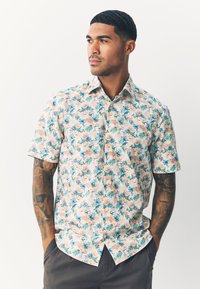 Camicia a maniche corte con bottoni, caratterizzata da un motivo floreale in blu, rosa e verde su uno sfondo chiaro. Realizzata in tessuto traspirante.