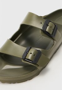 Sandale vert olive en plastique lisse avec deux sangles réglables et boucles noires. Comprend une semelle intérieure profilée et une semelle extérieure texturée.