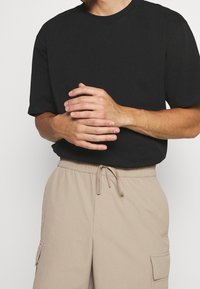Sort bomulds T-shirt med rund halsudskæring, parret med beige cargo shorts med snøre i taljen, som har sidelommer og en glat tekstur.