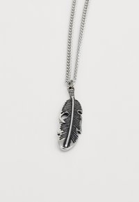 Pendentif en forme de plume en argent avec des détails gravés en noir sur une chaîne en argent, sur fond blanc uni.
