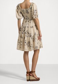 Blumenmusterkleid mit quadratischem Ausschnitt, Puffärmeln und gestuftem Rock. Hergestellt aus leichtem Stoff, mit beigem Grund und blauen Blumenmustern.