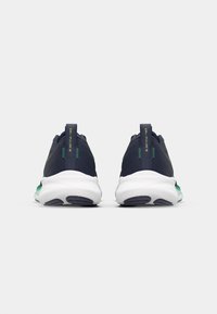 Marineblauwe sport schoenen met een bovenwerk van mesh, groene accenten en een witte middenzool, met een gewatteerde kraag en een gestructureerde zool voor grip.